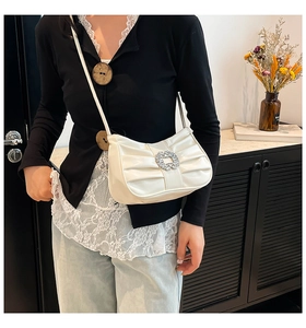 Detail of white pleated crescent bag featuring a large sparkling rhinestone buckle