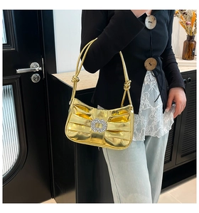 Detail of gold pleated underarm bag featuring a sparkling crystal square buckle design