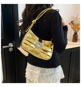 Detail of golden pleated underarm bag with a sparkling rhinestone buckle on a shoulder strap