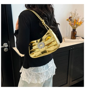 Detail of a metallic gold pleated shoulder bag featuring a large square crystal buckle