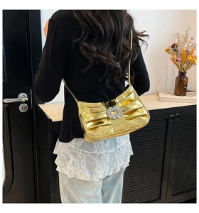 Detail view of a gold pleated shoulder bag with sparkling rhinestone buckle on a model