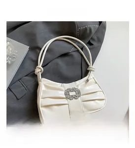 Close-up of cream white pleated shoulder bag with large rhinestone buckle and knot strap