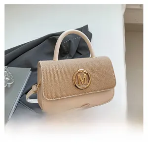 Détail du rabat tissé avec boucle dorée en M sur un sac boîte vintage beige