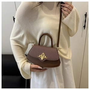 Detail einer braunen Patchwork-Handtasche mit goldener Schnalle und Perle auf beige Outfit