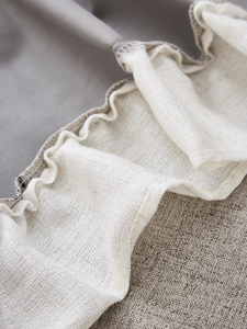 Detail of thick linen curtain fabric showing ivory pleated hem and grey weave texture
