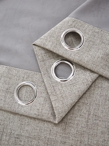 Close-up of thick linen curtains showing silver metal grommets and coarse woven texture