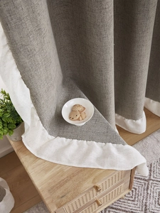 Detail of thick grey linen curtain featuring a decorative white ruffle hem on wood cabinet