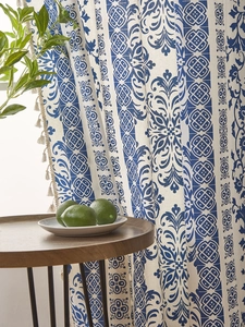 Close-up of blue and white floral patterned curtain with bohemian pompom fringe detail