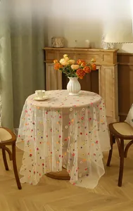 Close-up of vibrant floral embroidery on white lace mesh tablecloth with wavy edges