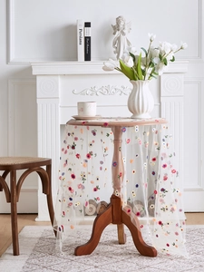 Detailed view of colorful floral embroidery on white lace mesh tablecloth over round wood table