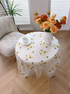 Detailed top view of white lace tablecloth with yellow floral embroidery on a round table