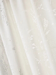 Dettaglio della tenda in pizzo bianco con delicato motivo floreale jacquard e pieghe