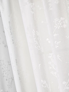 Détail de rideau en dentelle blanche avec motifs floraux et finitions à volants doux
