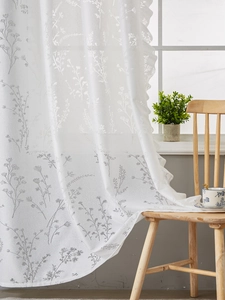 Détail du rideau en dentelle blanche avec motifs floraux gris et bordure festonnée