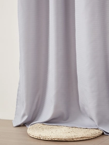 Detail of light purple sheer curtain with horizontal texture draping on wooden floor