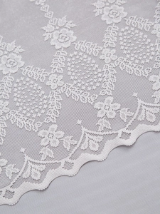 Macro detail of light grey floral lace sheer curtain with rose patterns and scalloped edges