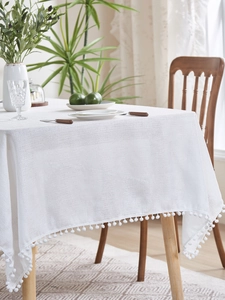 Detail of white linen tablecloth with decorative pom-pom trim in a cozy Nordic dining room