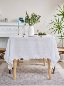 Detail of white linen tablecloth with decorative pom-pom fringe on a wooden dining table