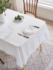 Close-up of white linen tablecloth featuring decorative pom-pom fringe and woven texture
