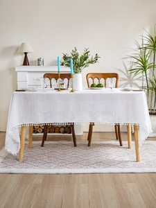 Detail of white textured tablecloth featuring decorative pom-pom fringe edges in a cozy home setting