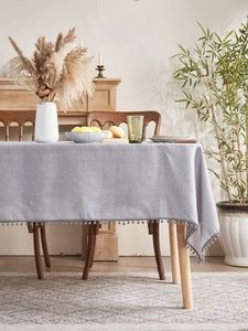 Detail of light gray textured tablecloth with decorative pom-pom fringe in Nordic home setting
