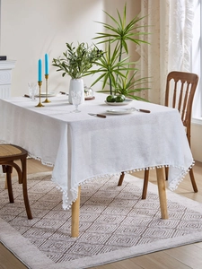 Detail of white textured tablecloth with soft pom-pom fringe in a Nordic dining setting