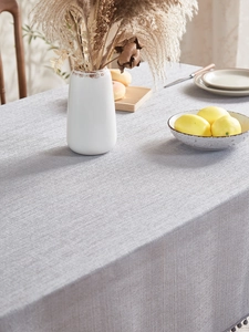 Close-up of light grey linen texture tablecloth with pom pom tassels in home setting