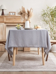 Detail of grey linen texture tablecloth featuring decorative pom-pom fringe trim edges