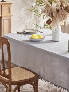 Detail of grey linen textured tablecloth featuring elegant pom-pom fringe edges