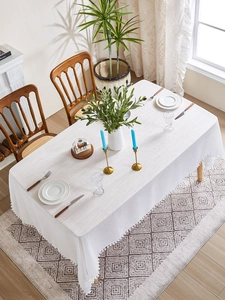 Close-up of white linen-textured tablecloth with decorative pom-pom fringe on edges