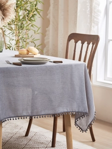 Close-up of grey textured tablecloth featuring delicate small pom-pom fringe details