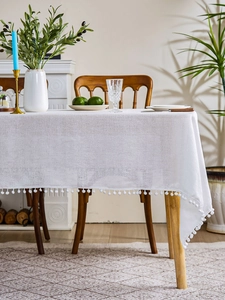 Close-up of white linen-textured tablecloth with decorative pom-pom fringe details