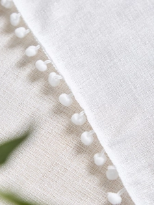 Close-up of white linen textured tablecloth with decorative pom-pom fringe details
