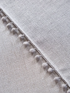 Detailed view of light grey textured linen tablecloth with decorative pom-pom fringe