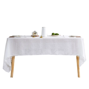White minimalist rectangular tablecloth with pom-pom fringe on a wooden table