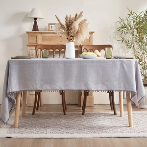 Nordic light grey rectangular tablecloth with pom-pom tassels on a wooden dining table