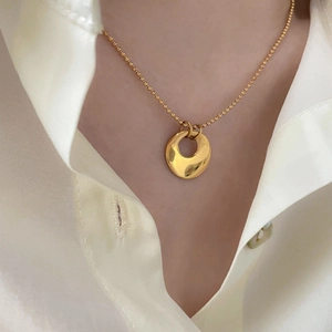Gros plan d'un collier pendentif doré porté par un mannequin en chemise de soie