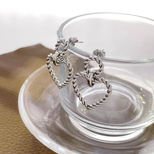 Detail of silver twisted rope heart earrings hanging on glass with vintage metallic texture