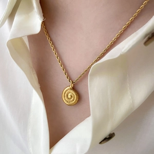 Gros plan d'un pendentif spirale dorée sur une chaîne torsadée porté sur une chemise
