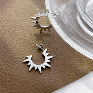 Macro detail of silver sun-shaped stud earrings with sharp radiating lines on leather