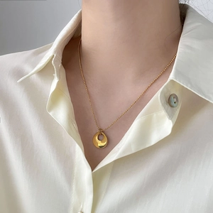 Gros plan d'un collier doré minimaliste avec pendentif rond creux porté par un mannequin