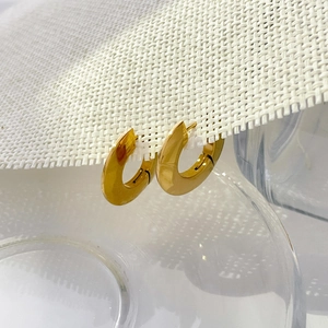 Close-up of chunky gold-plated hoop earrings with polished mirror finish on white mesh