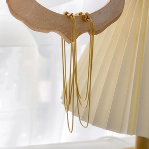 Detailed view of long gold tassel earrings with fine snake chains on a wooden display