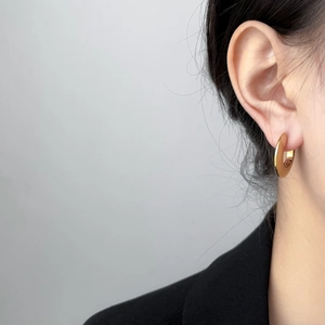Close-up of golden chunky hoop earrings worn by a model with a black blazer and gray backdrop