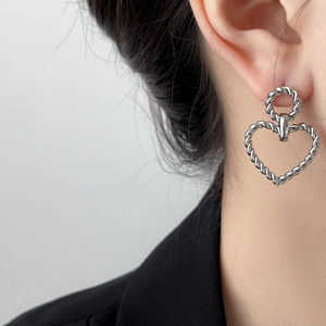 Close-up of silver twist texture hoop earrings with hollow heart pendants on model