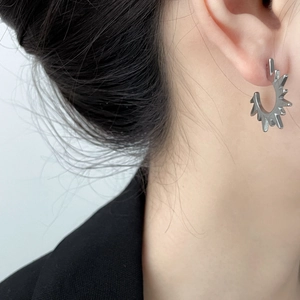 Detailed close-up of a silver C-shaped earring with sunburst spikes on earlobe