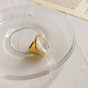 Détail macro d'une bague dorée avec nacre en forme de goutte dans un plateau en verre
