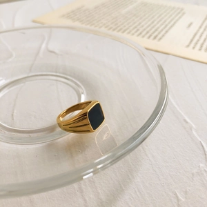 Détail d'une bague chevalière carrée en émail noir doré posée sur un plateau