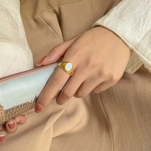 Détail de la bague chevalière vintage dorée avec nacre blanche ovale sur la main