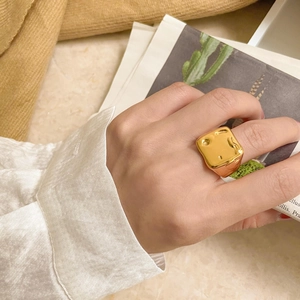 Gros plan d'une bague large dorée avec texture de lave portée par un mannequin de mode